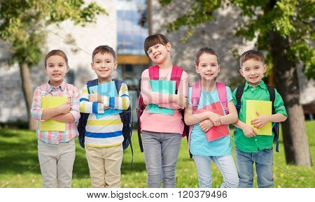 childhood, preschool education, learning and people concept - group of happy smiling little children with school bags and notebooks over summer campus background