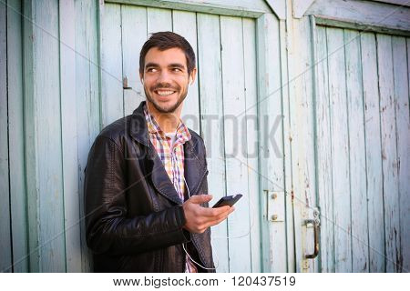 Young man listening to music on a house wall background
