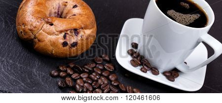 Roasted Coffee Beans With Drink And Bagel In Background On Slate Stone