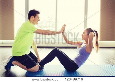 fitness, sport, training, teamwork and people concept - happy woman with personal trainer doing sit ups and high five gesture in gym