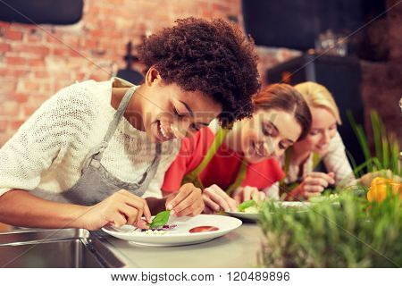 cooking class, friendship, food and people concept - happy women cooking and decorating plates with dishes in kitchen