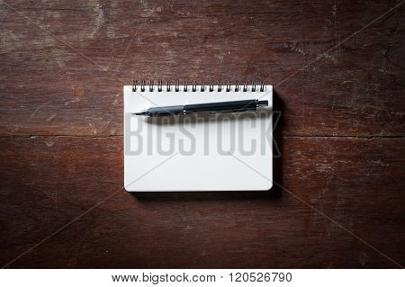 Small opened notepad with blank area for text or message and pen on rustic wood table with low key scene.