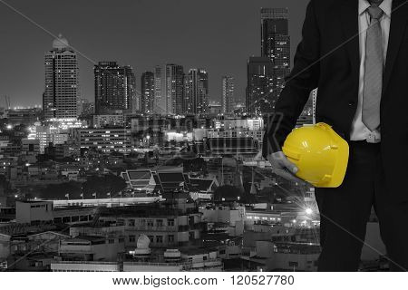 Engineer holding a yellow helmet for the safety of the workers, with city as a backdrop and modern b