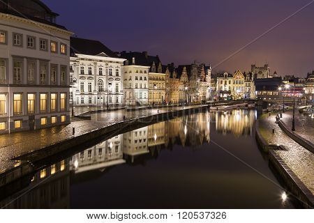 A view of beautiful old buildings along Korenlei and the River Leie in Ghent Old Town at night. Reflections can be seen in the water.