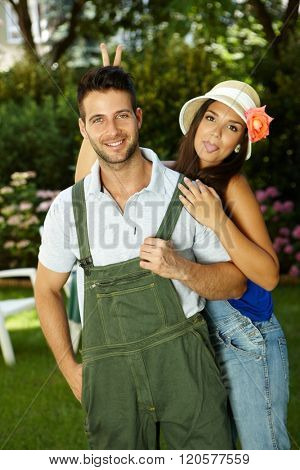 Young couple having fun in the garden, woman sticking tongue, smiling happy.