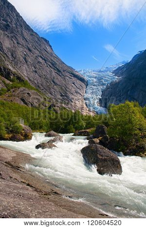 Norway. Summer day at a glacier Briksdal. A stream of thawed snow against mountains and a glacier