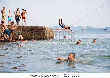 NAKHODKA, RUSSIA - CIRCA AUGUST, 2015: Joyful children jumping and diving into the sea from the old dock. Local children love to relax, sunbathe, swim and dive in the sea bay near the Nakhodka city