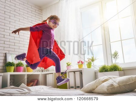 Child girl in an Superman's costume plays. The child having fun and jumping on the bed.