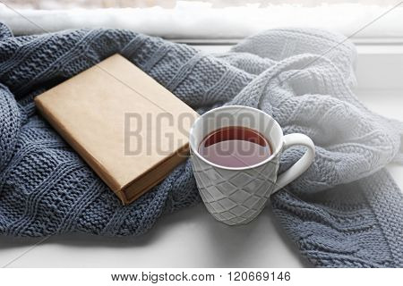 Cup of tea, book and warm knitted plaid on windowsill, close up