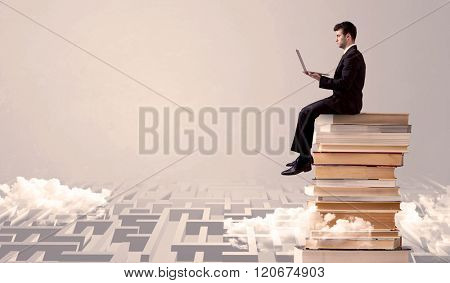 A businessman with laptop tablet in elegant suit sitting on a stack of books on top of sandy labirynth background concept