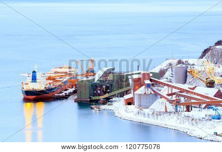 Industrial Container Cargo freight ship with working crane bridge in shipyard at Iron Ore Mine Factory Plant in Narvik Norway