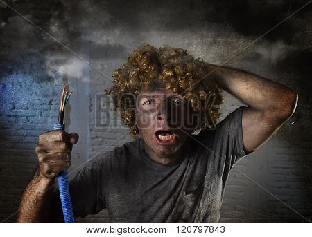 young man with funny curly wig holding electrical cable smoking after domestic accident with dirty burnt face and shock electrocuted expression in electricity DIY repairs danger concept in black smoke background
