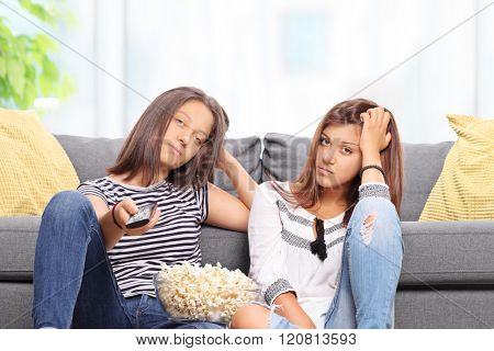 Bored teenage sisters watching TV and changing the channels isolated on white background