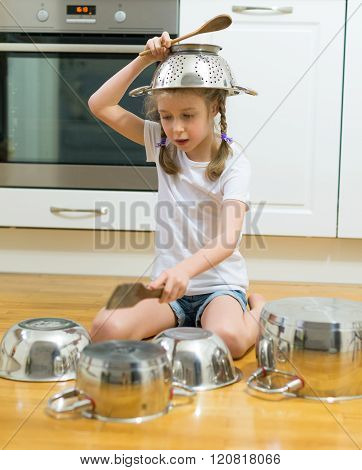 Little girl playing drums on pots and pans in the kitchen.
