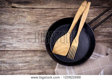 Frying pan and kitchen utensils on wooden table background