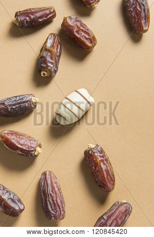 A date fruit coated with white chocolate amongst scattered ripen dates. 'Unique' or 'different' concept.