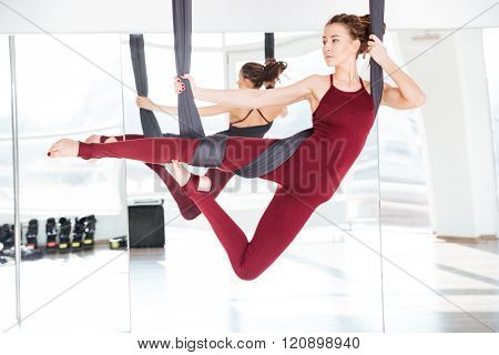 Concentrated beautiful young woman practicing different antigravity yoga positions over the mirror