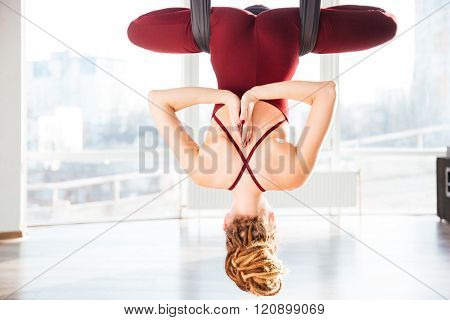 Back view of attractive young woman doing pose of antigravity yoga in studio