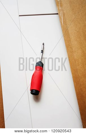 Screwdriver on a board in the process of setting up recently purchased furniture. Tilt shift-lens intentionally used for a better focus on the object.