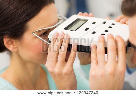 health care, medicine, people, eyesight and technology concept - close up of optometrist with pupillometer checking patient intraocular pressure at eye clinic or optics store