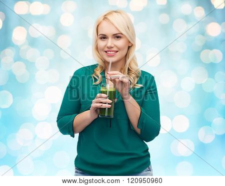 healthy eating, vegetarian food, diet, detox and people concept - smiling young woman drinking green vegetable juice or smoothie from glass over blue holidays lights background