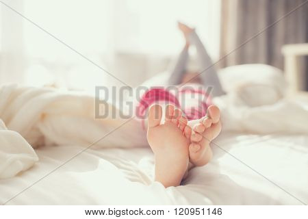 Bare feet of a child,a little girl,waking up in the morning on a big white bed in his bedroom in front of the window,the girl is lying on a white soft blanket,the child stretches himself,raising his hands