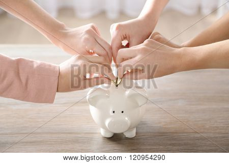 Hands putting coin into piggy bank at the table