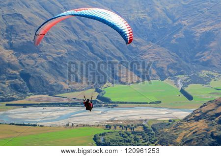 Paragliding sportsman flying high over mountains with a parachute wind break, gliding over fields with the wind