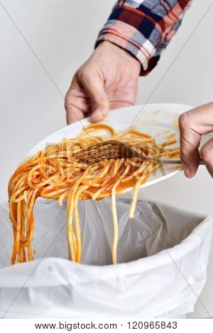 closeup of a young man throwing the leftover of a plate of spaghetti to the trash bin