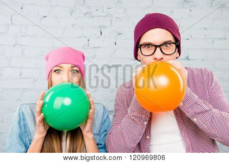 Portrait of attractive man and woman in hats inflating balloons