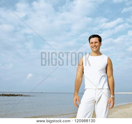 young brunette man on beach at sea smiling, gomosexual in white