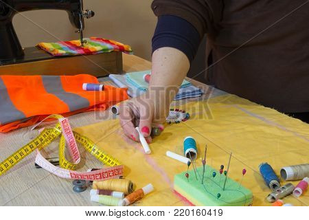 Couturier sews a dress in the studio. Fashion designer making a pattern on piece of tissue. Sewing machine is standing on the table beside them. Workplace of seamstress