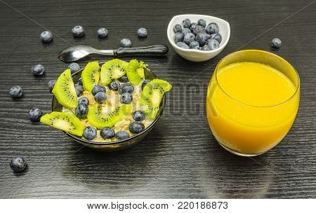 Breakfast for a child. Oatmeal on milk with fruits (blueberries and kiwi) and a glass with orange juice to drink.