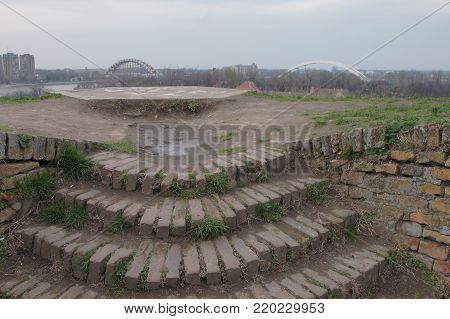 The arches of the bridge dominate the horizon. Bridge under construction is best seen from spot for observation. The observation stairways are made of bricks. Everything points to great endeavor and success.