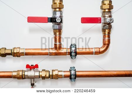 Copper pipes and valves on a white wall. Close up.