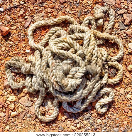 Old thick rope with tied knots rolled on the ground. Thick is unwound from the time the rope lies on the red clay soil. Tinted