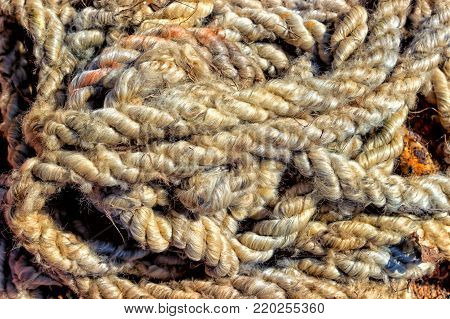 Old thick rope with tied knots rolled on the ground. Thick is unwound from the time the rope lies on the red clay soil. Tinted