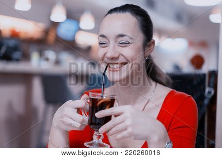 Beautiful smiling girl in red dress drinks mulled wine at coffee shop. toned