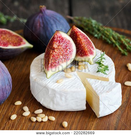 Camembert cheese with figs and pine nuts on wooden cutting board. Close up view, square composition