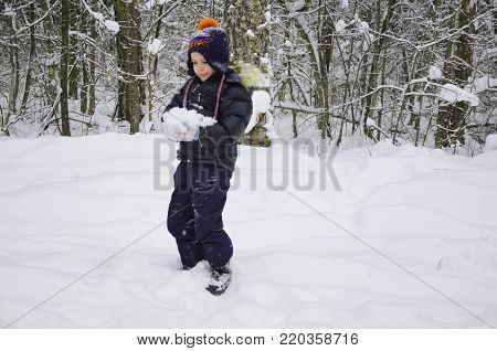 A simpotic little boy throws snow in the winter snow-covered forest, trees in the snow. enjoys the winter. plays snowballs. happy, smiling, laughing with falling snow