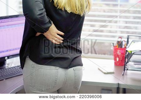 Close-up view of a young woman with pain in kidneys. Young woman with back ache clasping her hand to her lower back. Woman suffering from ribbing pain, waist pain.