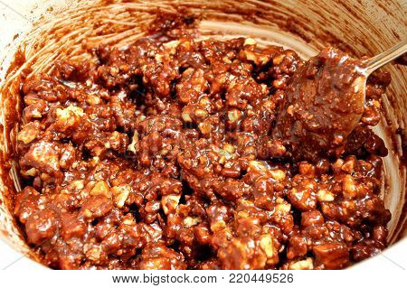 Process of cooking chocolate mass with walnuts and cookie crumbs in a white saucepan. Top view, close-up.