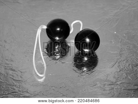 Simple cheap black vaginal love balls on silver shiny surface. Sex toy object.