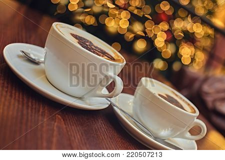 Two white cups with aroma refreshing coffee on a table with illumination lights on the background.