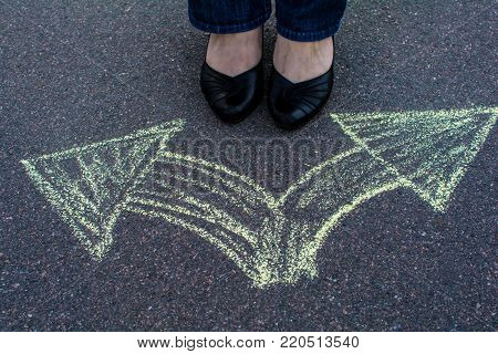 Woman in shoes standing on the asphalt road. On the road with chalk drawn signs arrows.