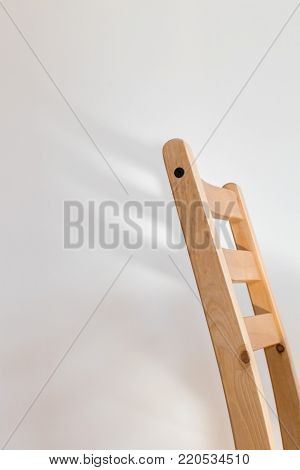 Chair dreaming of wings; the back of a wooden chair casts a wing-shaped shadow on a clean white wall behind it