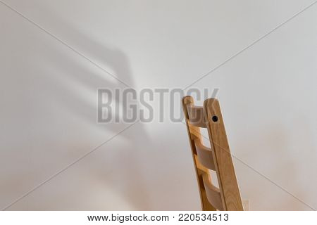 Chair dreaming of wings; the back of a wooden chair casts a wing-shaped shadow on a clean white wall behind it