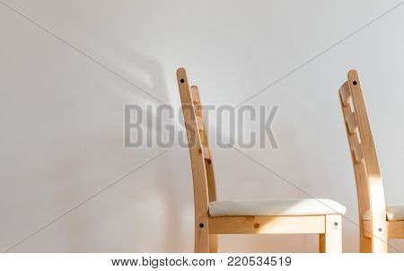 Chair dreaming of wings; two wooden chairs before a clean white wall, the back of one of casts a wing-shaped shadow