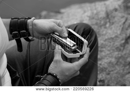Male hands hold a harmonica. Close-up. Outdoors. Black and white.