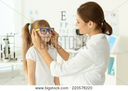 Cute little child trying on new glasses in ophthalmologist's office